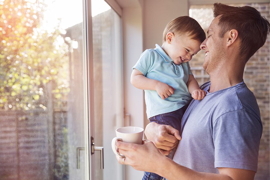 Personal Insurance - Happy Father Holds Toddler Son in Front of Patio Door While Drinking Coffee at Home